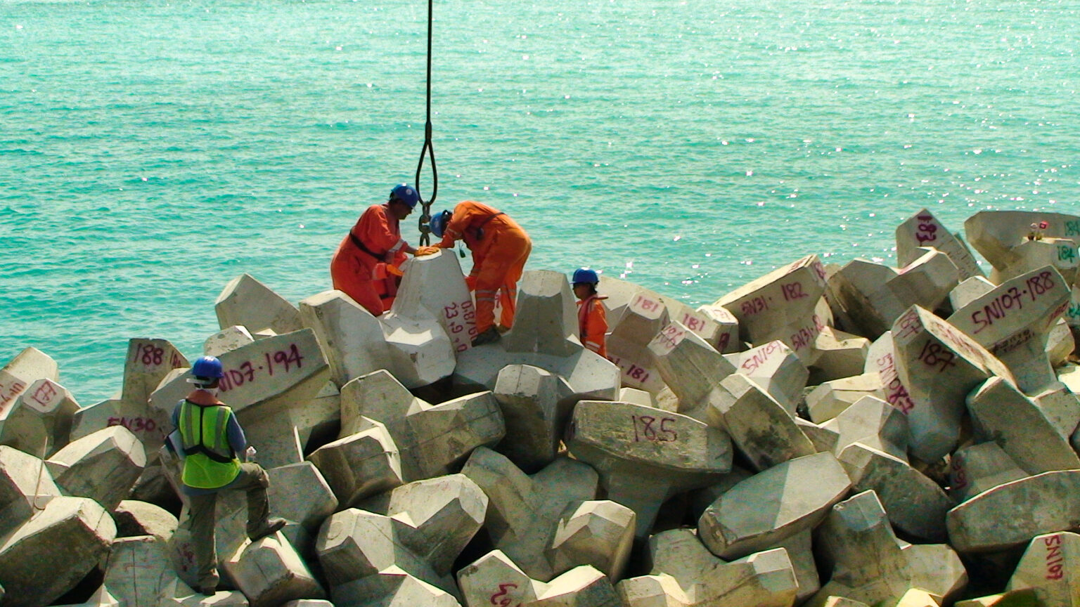 Pose d’un bloc de carapace sur la digue sous le contrôle des experts CLAS pour garantir une mise en place précise et stable.