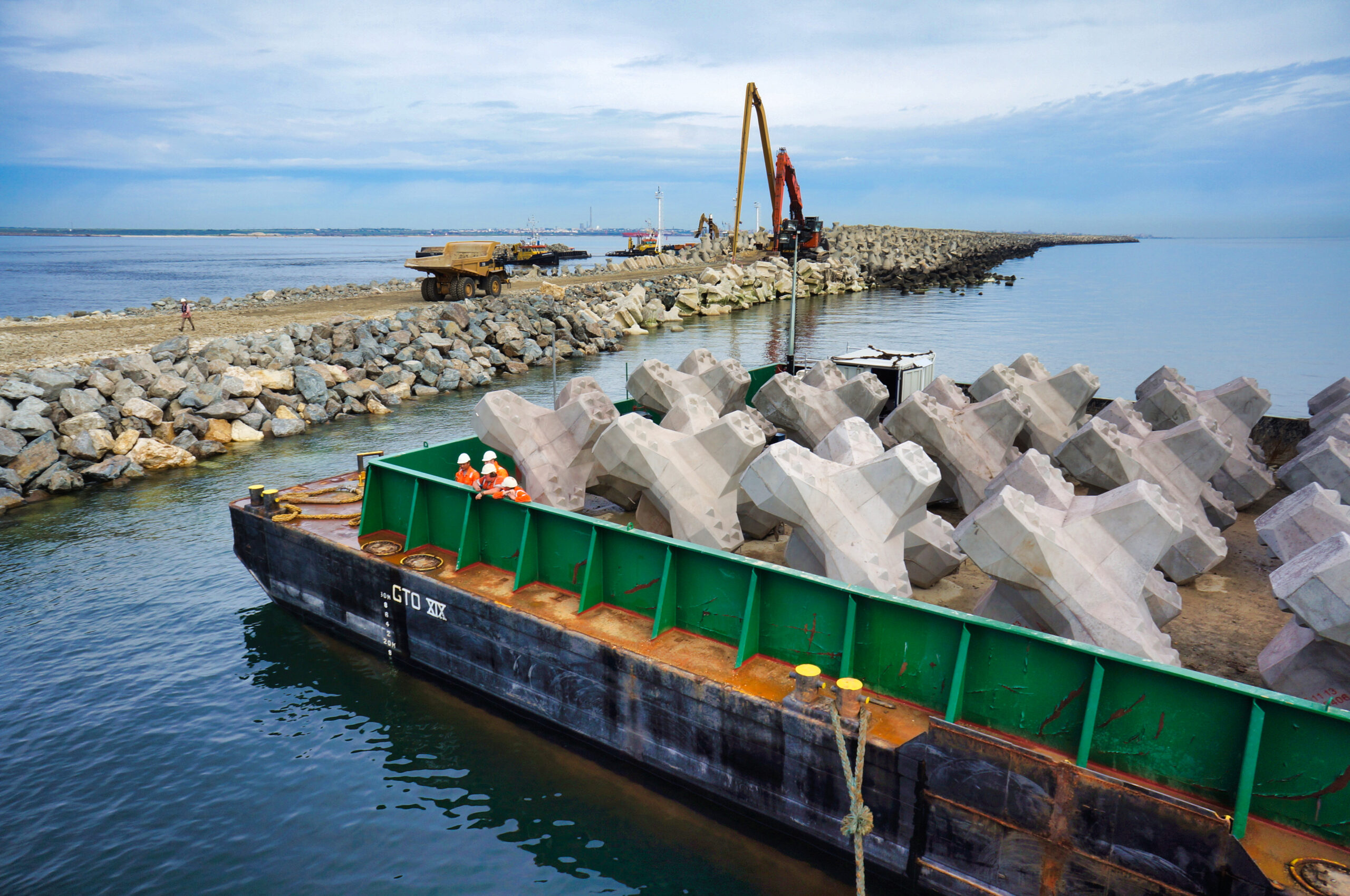 Barge de chantier acheminant les blocs de carapace vers la digue pour leur mise en place sous supervision CLAS.