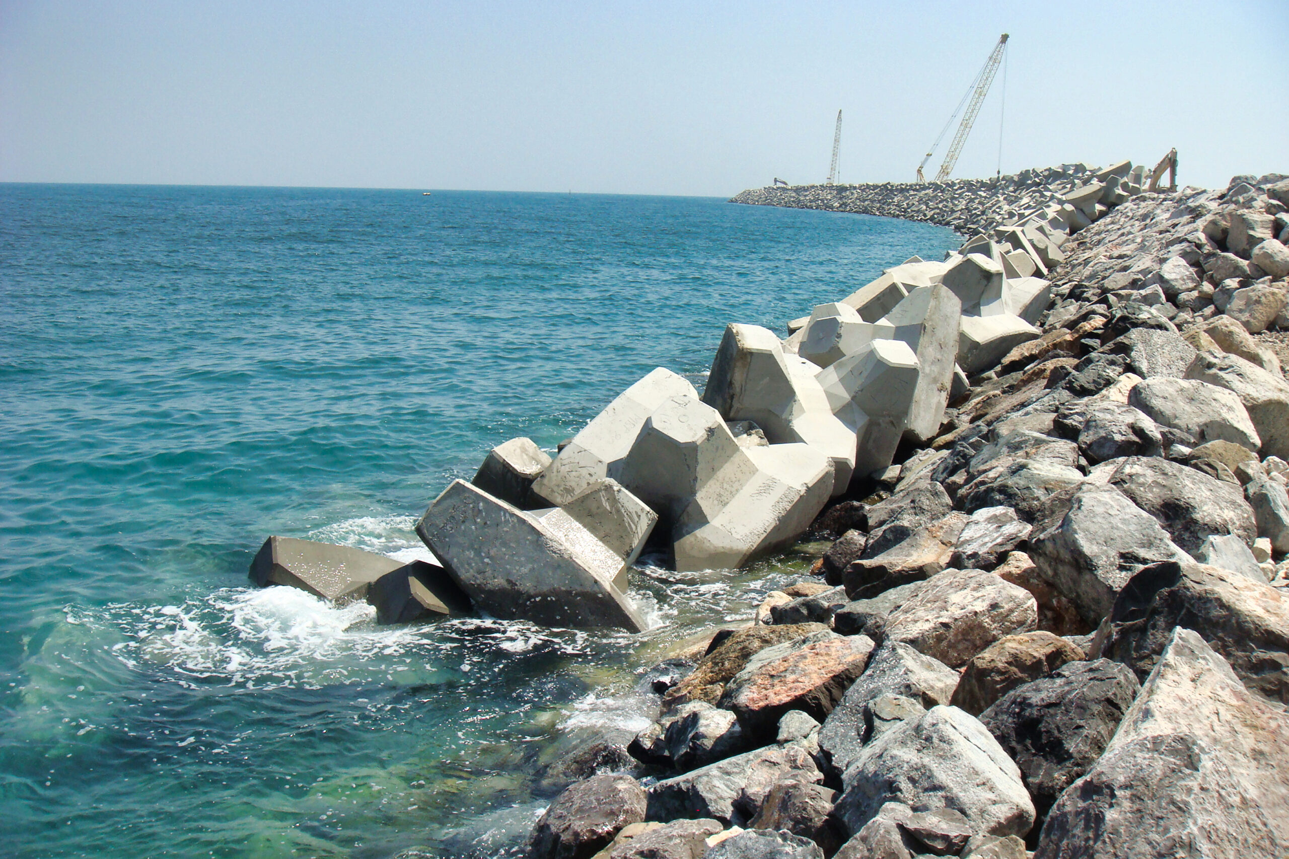 Vue de la carapace de la digue en construction avec des blocs artificiels en cours de mise en place.
