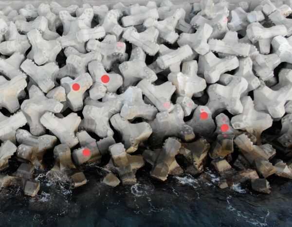 Groupe de cinq blocs cassés visibles sur la digue de la Nouvelle Route du Littoral, révélant une zone fragilisée nécessitant une inspection approfondie.